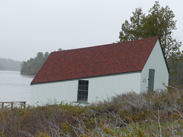The white boat house with red roof on the bank of the Kennebunk River in Maine.